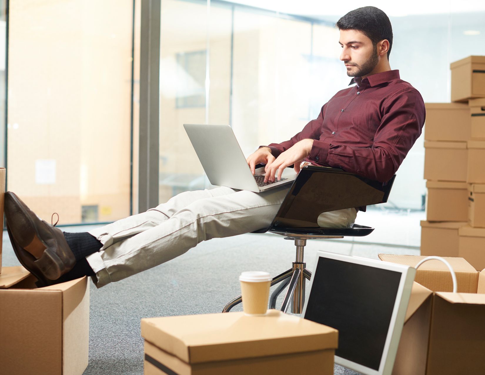 Male business owner in stock room typing on laptop with coffee